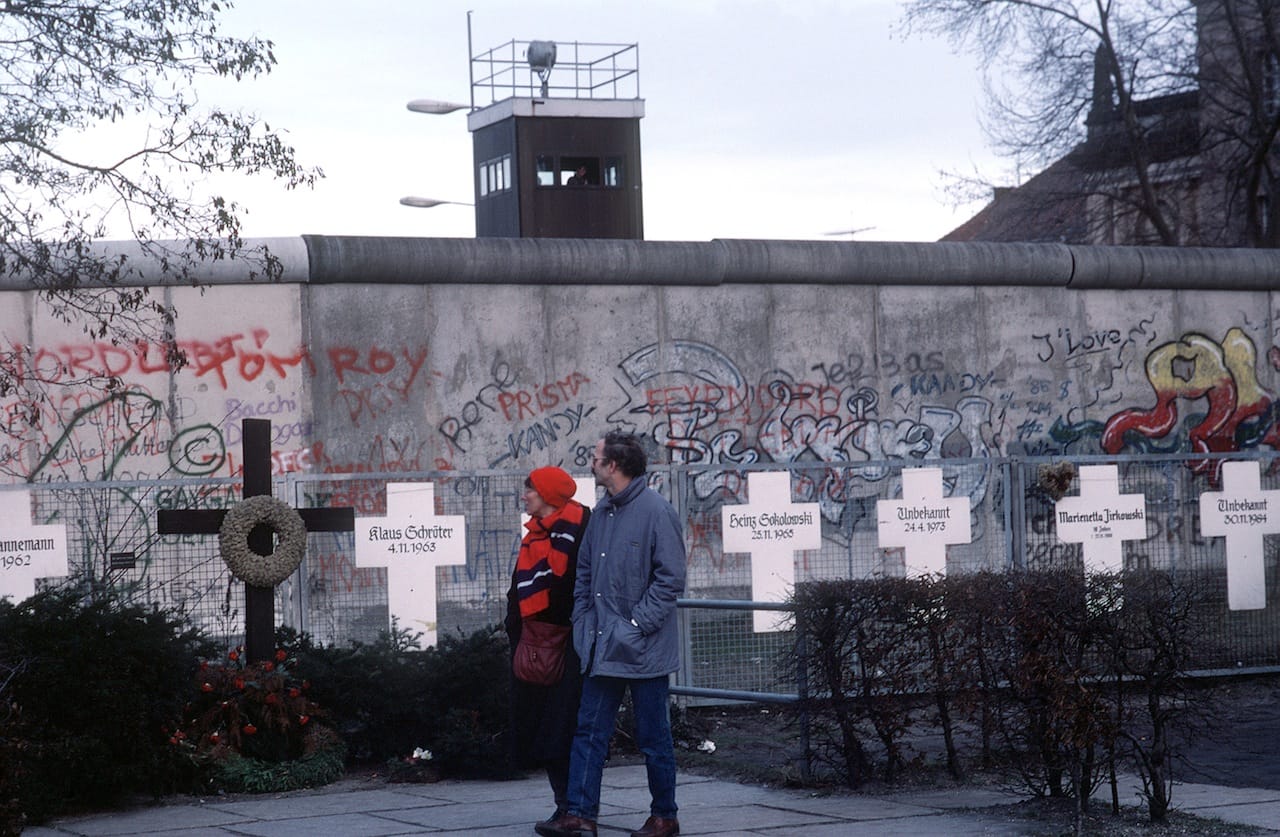 The White Crosses memorial on a fence in front of the Berlin Wall, where they were first installed in 1971. (Image via Wikimedia)