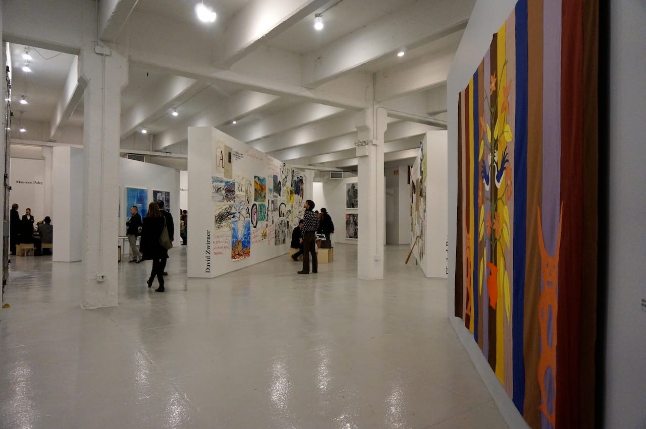 A view of Independent Projects, with a felt banner by Mike Kelley on the right and David Zwirner's booth of Raymond Pettibon in the center back