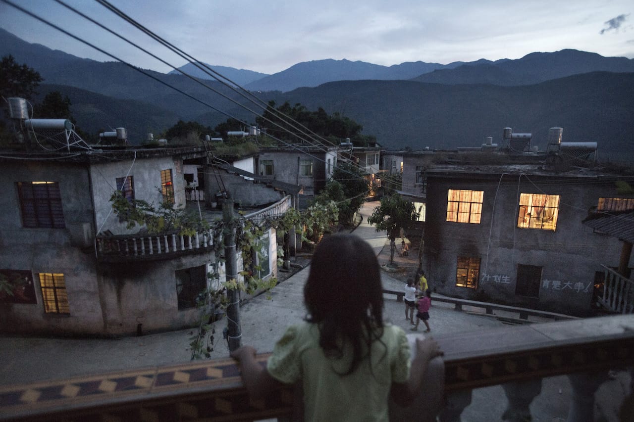 7-year-old Xiao Yuan looks at her village on a balcony at a neighbor's home in Yangxi village. Her mother gave birth to her at the age of 17. Xiao Yuan hasn't started school yet while the admission age is 6. Zhemi county, Yunnan province, China, October 27, 2014. © Muyi Xiao. All images courtesy of the Magnum Foundation.