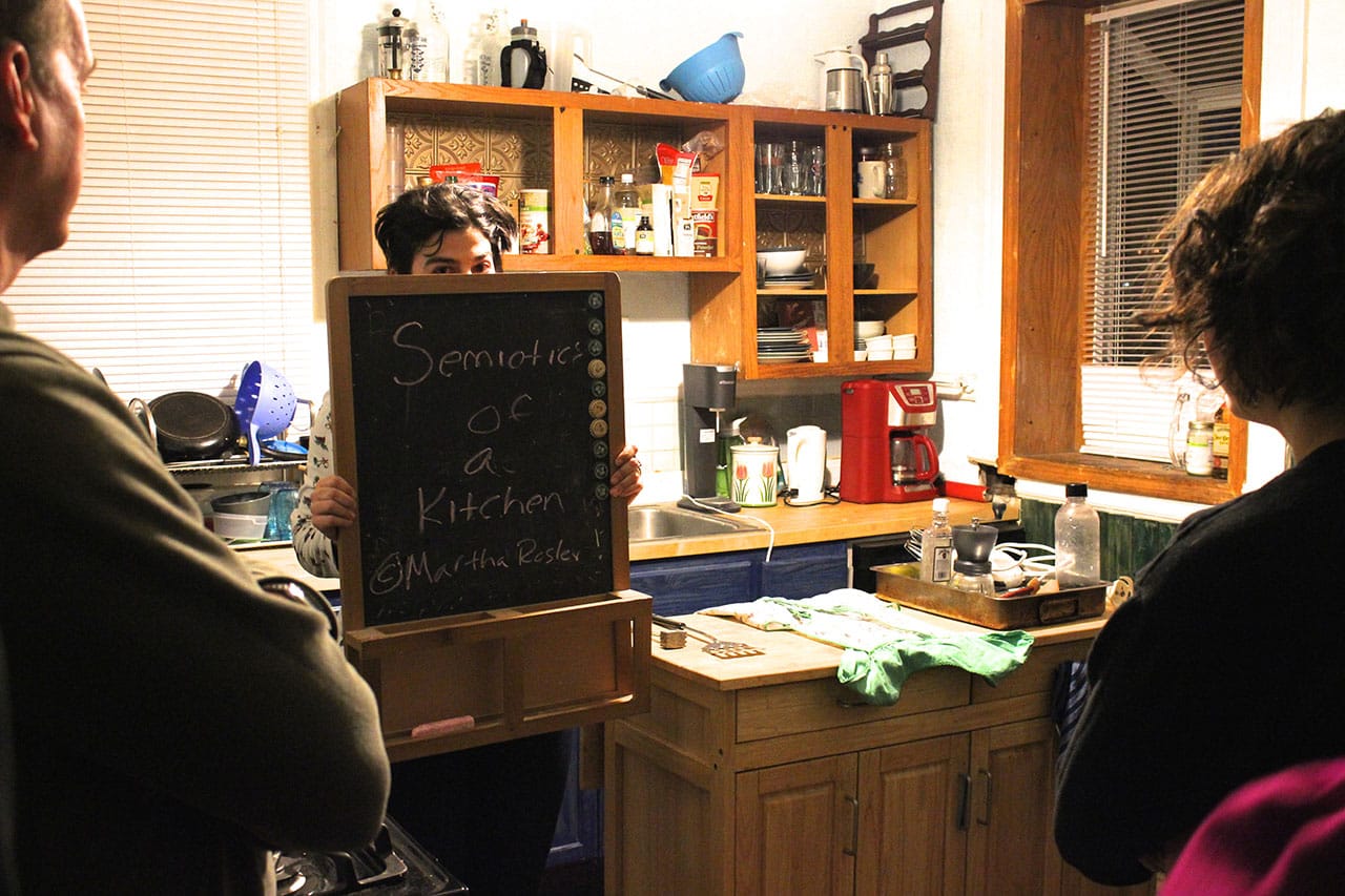 Eleni Zaharopoulos re-creating Martha Rosler’s “Semiotics of the Kitchen” (1975) in an actual kitchen, in A Host of People's 'The Modern Woman' (click to enlarge)