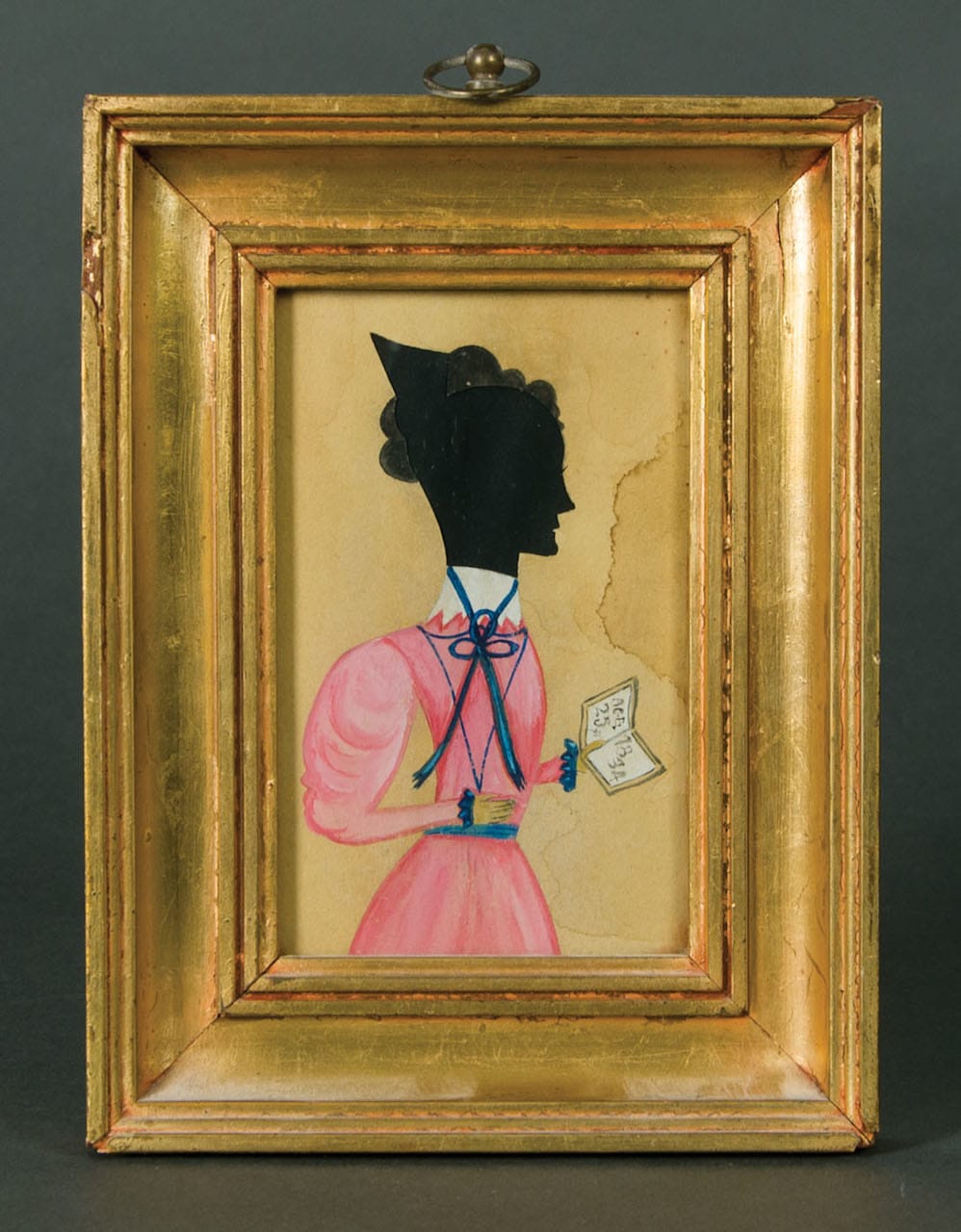 19th-century hollow-cut and watercolor silhouette of a young lady in a rose pink dress with blue ribbons and white collar, holding a book with "age 25 yrs, 1834," attributed to the "Puffy Sleeve" Artist