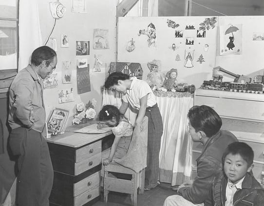 Ansel Adams, "Manzanar, CA, 1943" (1942).&nbsp;Photographer and incarceree Tōyō Miyatake who became an Adams friend and collaborator, in his children's bedroom, looking at daughter Minnie drawing, with his wife Hiro standing behind her. Eldest son Archie, near right, continued the family business, as did, for some time, sons Richard, far right, and Robert, not pictured (photograph by Ansel Adams, courtesy the Library of Congress, Prints & Photographs Division [reproduction no. LC-DIG-ppprs-00235])