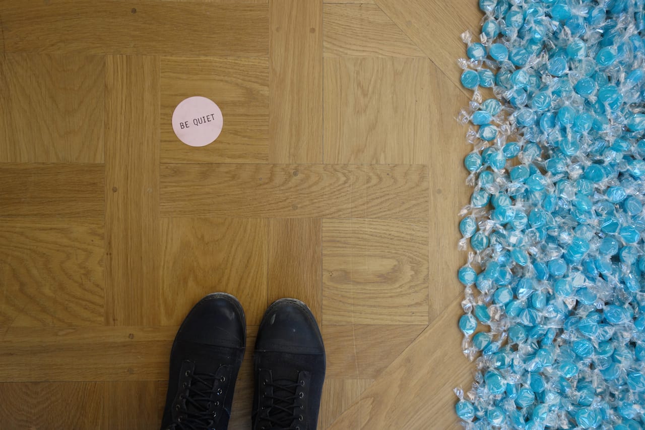 One of James Lee Byars's "Be Quiet" (1980) confetti pieces distributed by a performer with candy from Felix Gonzalez-Torres's "Untitled (Revenge)" (1991)