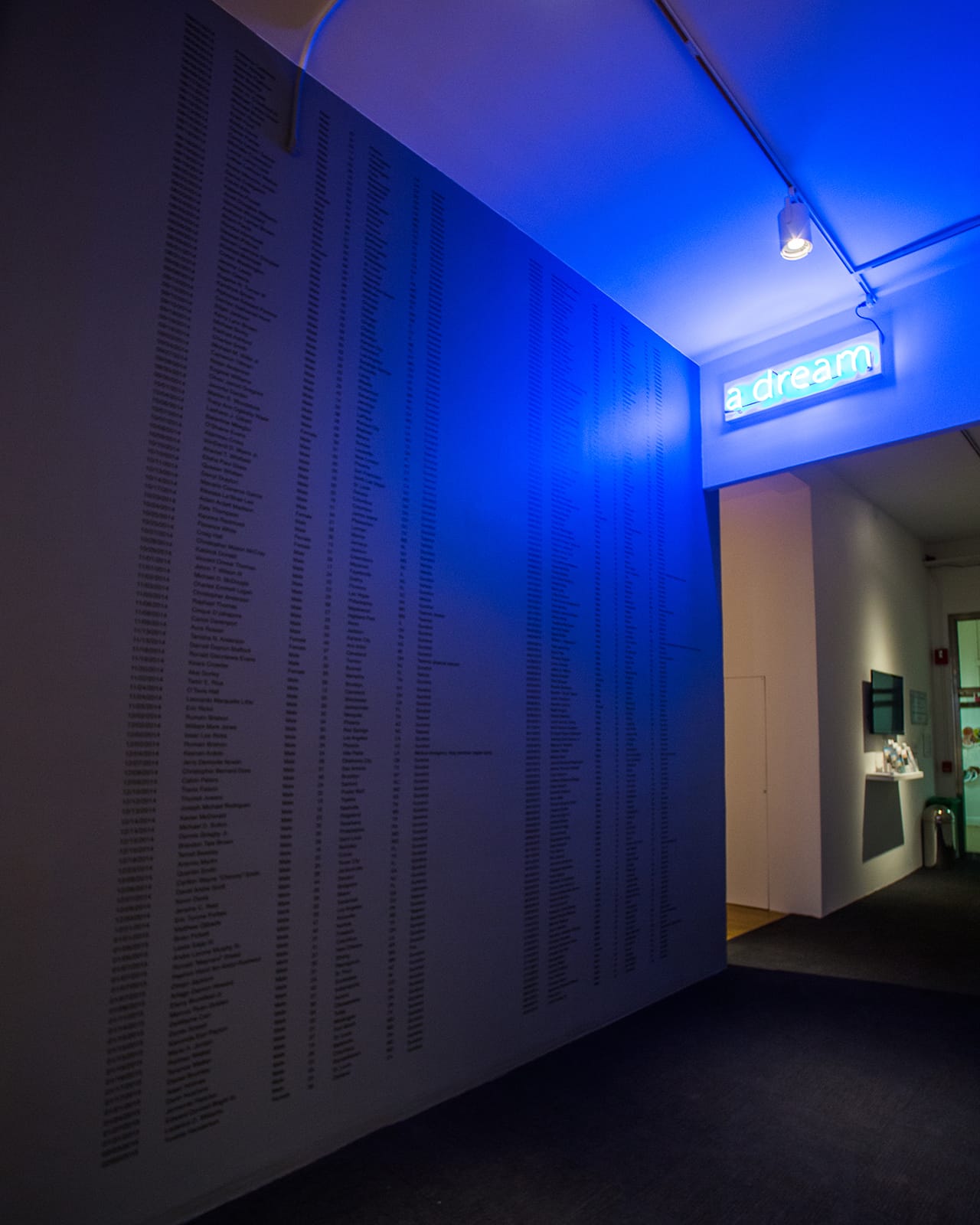 Steve Locke, "A Partial List of Unarmed African-Americans who were Killed by Police or who Died in Police Custody During my Sabbatical from Massachusetts College of Art and Design, 2014-2015" (2016), paint on wall with vinyl text, neon, dimensions variable