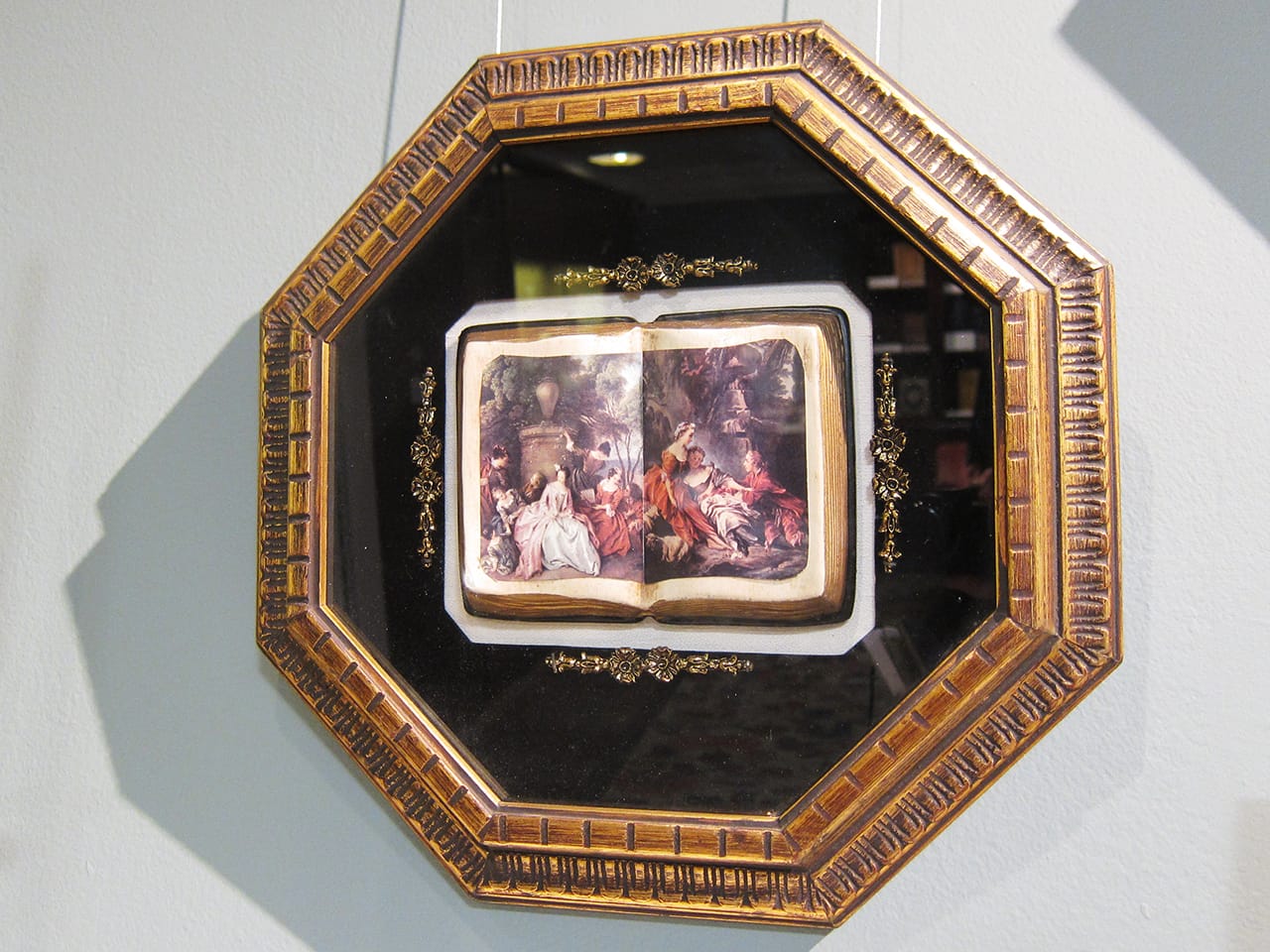 A framed faux box with three-dimensional open books showing decoupage images of famosu European paintings (mid-20th c.)