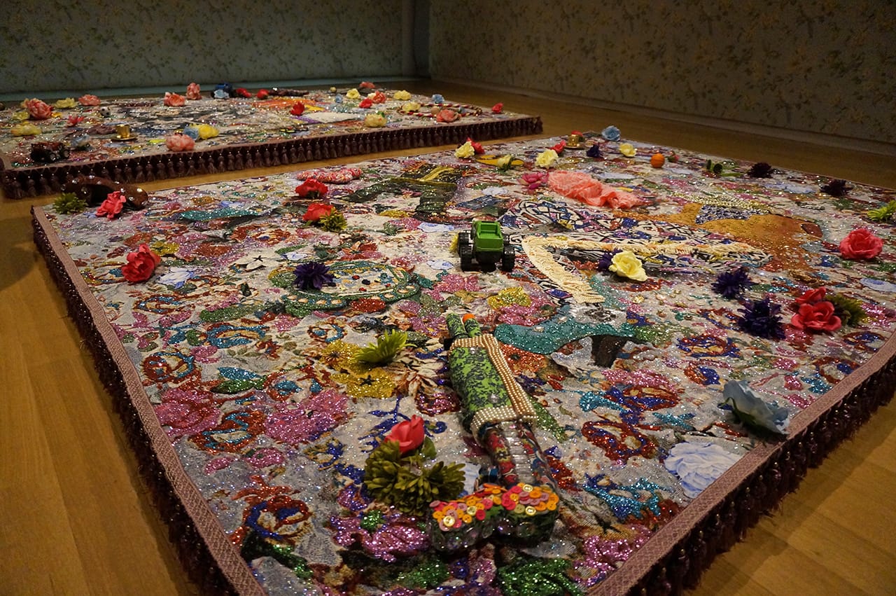 Installation view, ‘Ebony G. Patterson: Dead Treez’ at the Museum of Arts and Design; in foreground: “root and shrubz” (2014), mixed-media jacquard photo tapestry with embroidery, glitter, toy gun, shoe, lace, glasses, toys, silk flowers, embellishments (all photos by the author for Hyperallergic) (click to enlarge)