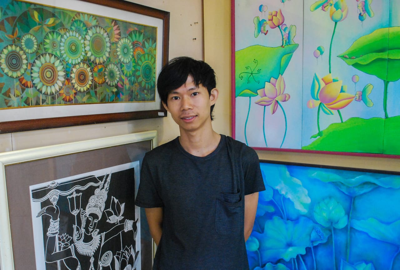 Painter and teacher, Hay Chhoem, stands with a few of his paintings on the left.