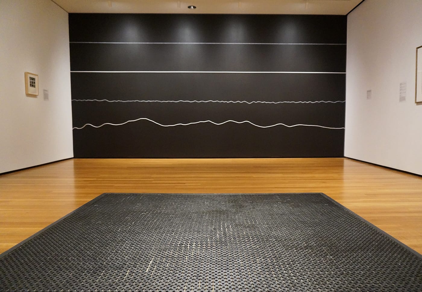 Foreground: Eva Hesse, "Washer Table" (1967), rubber washers, painted wood, and metal; background: Sol LeWitt, "Wall Drawing #325: On a black wall, white horizontal lines: two straight—one crayon, one wood; two not-straight—one crayon, one rope. The lines are equally spaced" (1980), white crayon, white wood, white rope on black wall