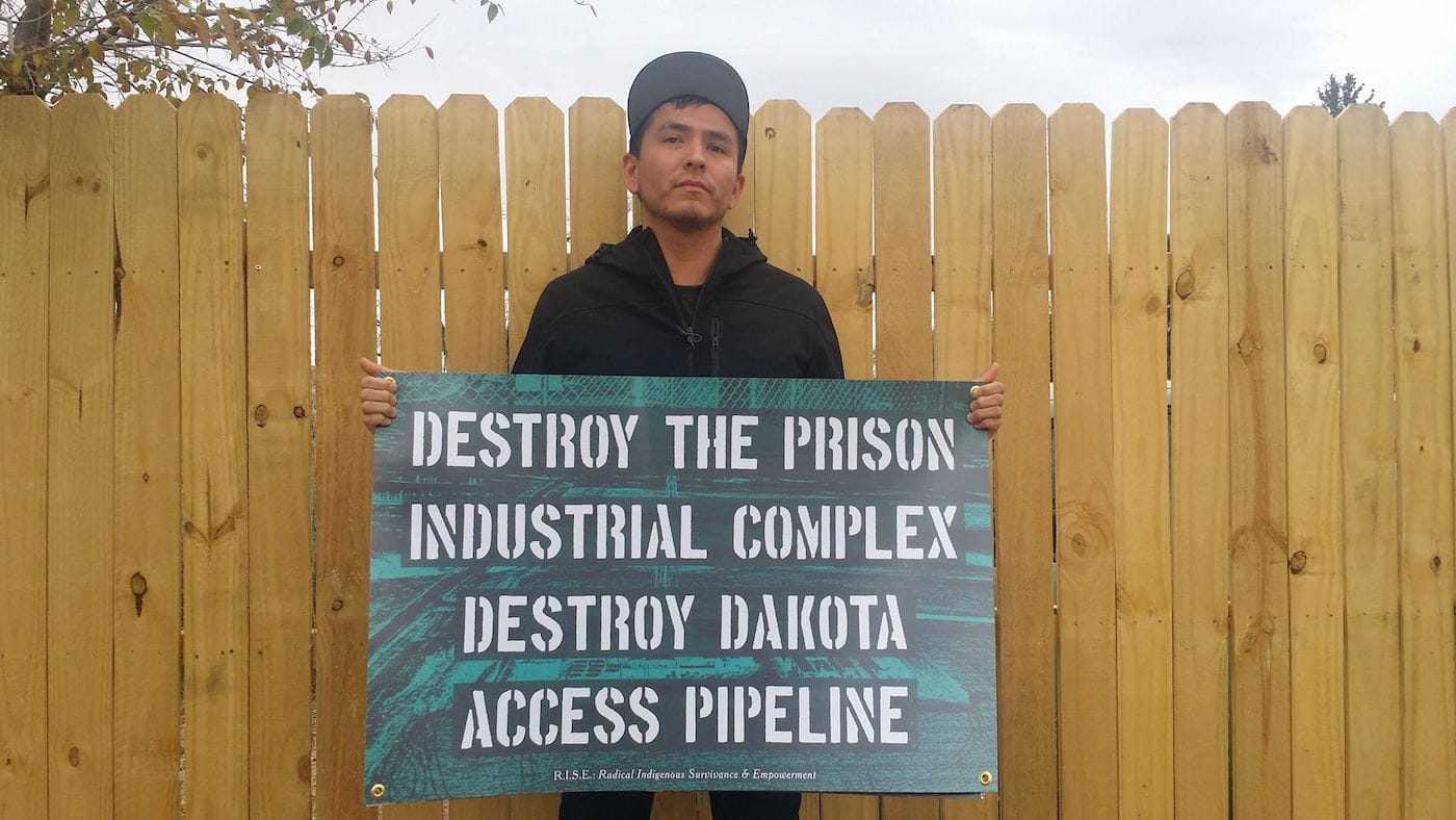 Demian DinéYahzi holding protest sign of his own creation (image courtesy of Cannupa Hanska Luger)