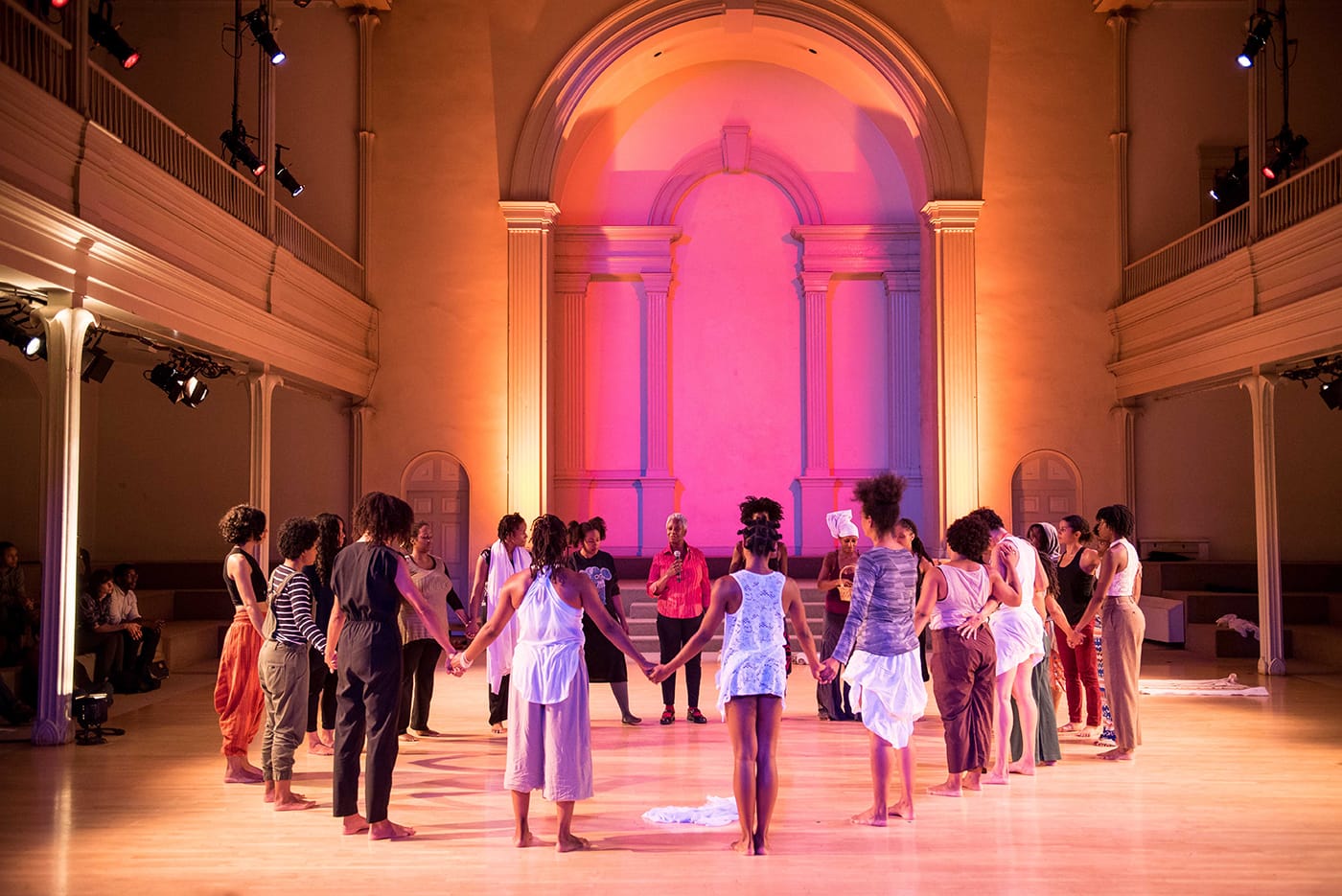 The performers gather in a circle at the end of the performance, with Eva Yaa Asantewaa (center, in red). the skeleton architecture, or the future of our worlds, Danspace Project. Photo: Ian Douglas/courtesy Danspace Project. 