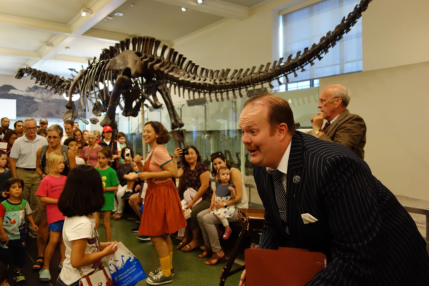<em>Rhoda and the Fossil Hunt</em> in the Hall of Saurischian Dinosaurs at the American Museum of Natural History (photo by the author for Hyperallergic)
