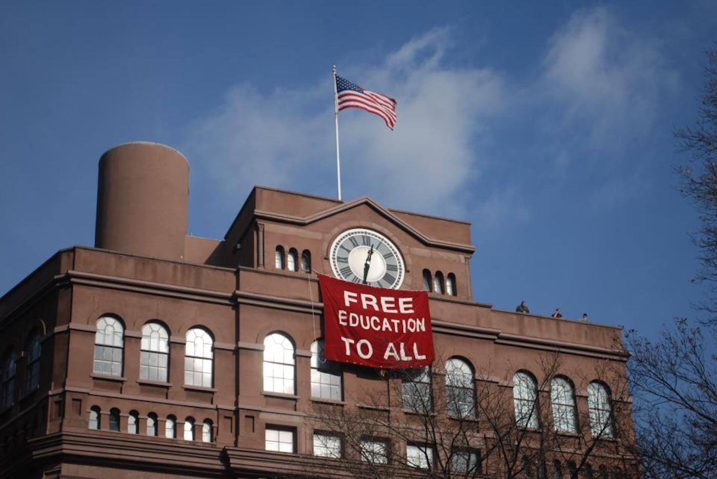 Students hang banner below the historic clock tower of the Cooper Union Foundation Building in December 2012. (photo by Free Cooper Union, via Wikimedia Commons)