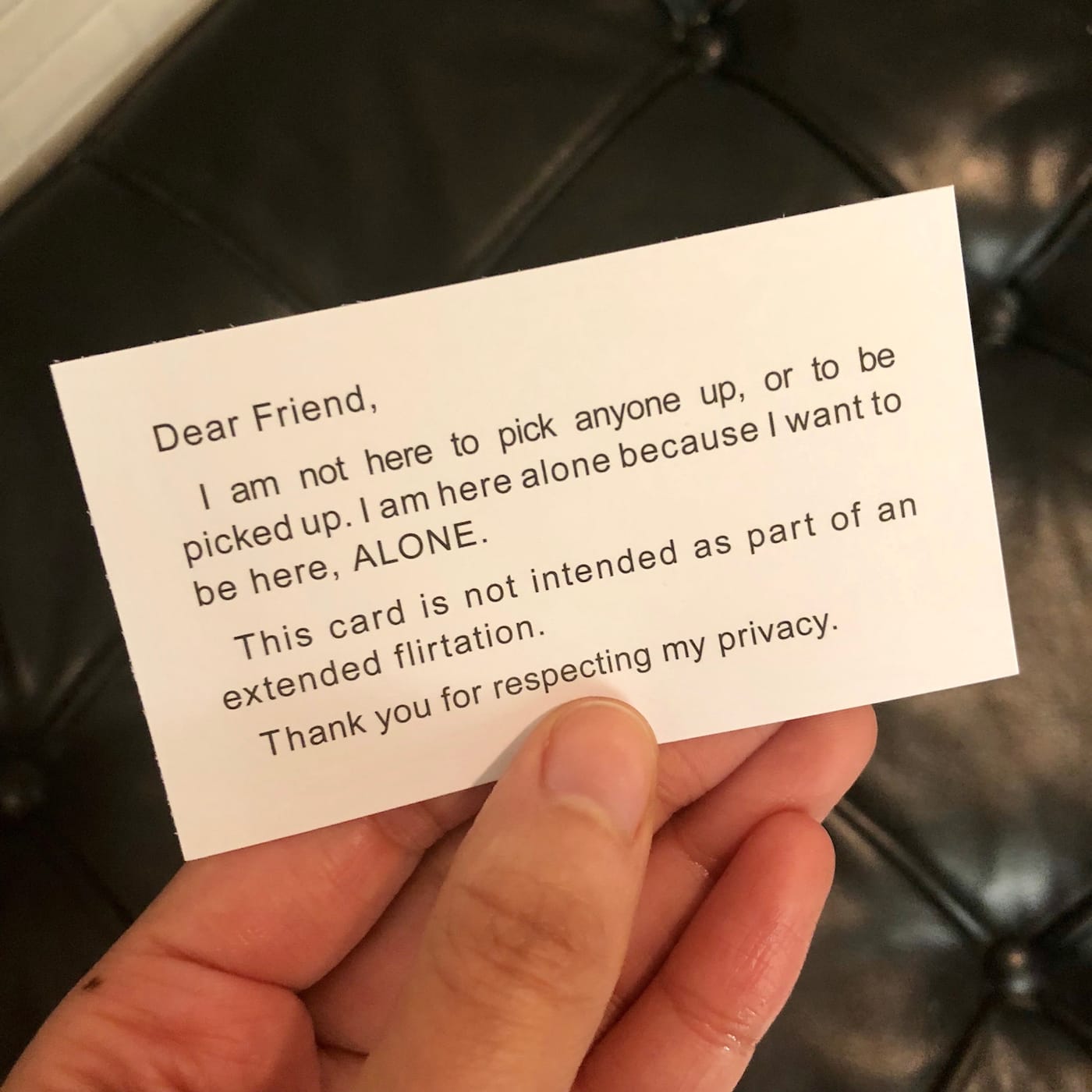 The author holding a copy of Adrian Piper's "My Calling (Card) #1" (1986–90) (photo by the author for Hyperallergic)