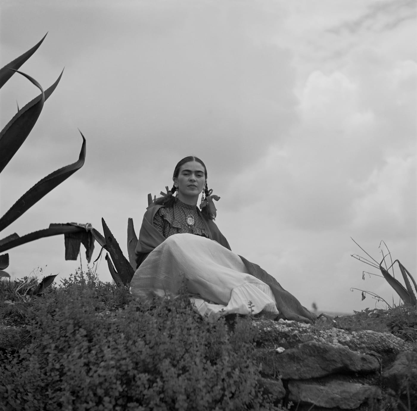 Frida Kahlo, seated next to an agave plant, from a 1937 photo shoot for <em>Vogue</em> titled "Señoras of Mexico" (photo by Toni Frissell, via Wikimedia Commons)