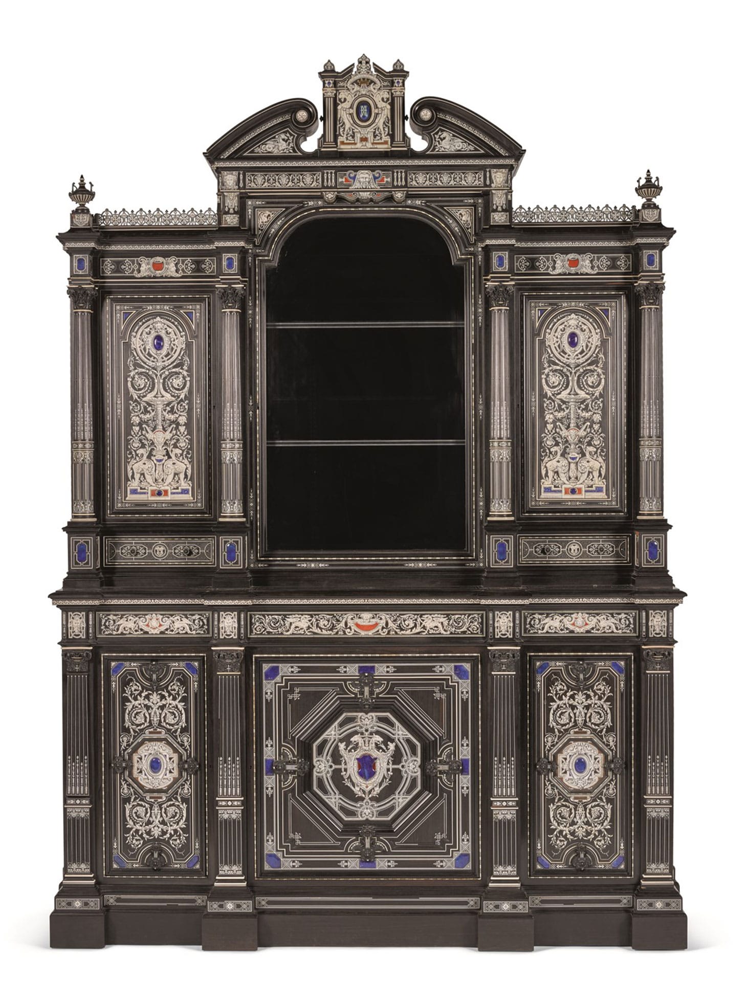 An important Victorian ivory and hardstone inlaid ebony cabinet designed by Alfred Lorimer for Jackson and Graham (c. 1867), of architectural form in Italian Renaissance style, the stepped upper section with broken arch pediment centred by a mythical coat-of-arms with a yellow gold crown over a pale blue enamelled 'K' monogram on a lapis ground, the arched panel glazed door flanked by two pairs of Corinthian columns with carved capitals and two panel doors, each over a short drawer, the lower section with moulded edge over four fluted Corinthian pilasters, flanking three panelled doors, on a plinth base, stamped Jackson & Graham to carcase in several places, the locks stamped by Chubb & Co., Makers to Her Majesty, No.596210, the reverse with fragment of lot entry from 1885 sale catalogue 112 x 83 x 25¾ inches (image courtesy Sotheby's)