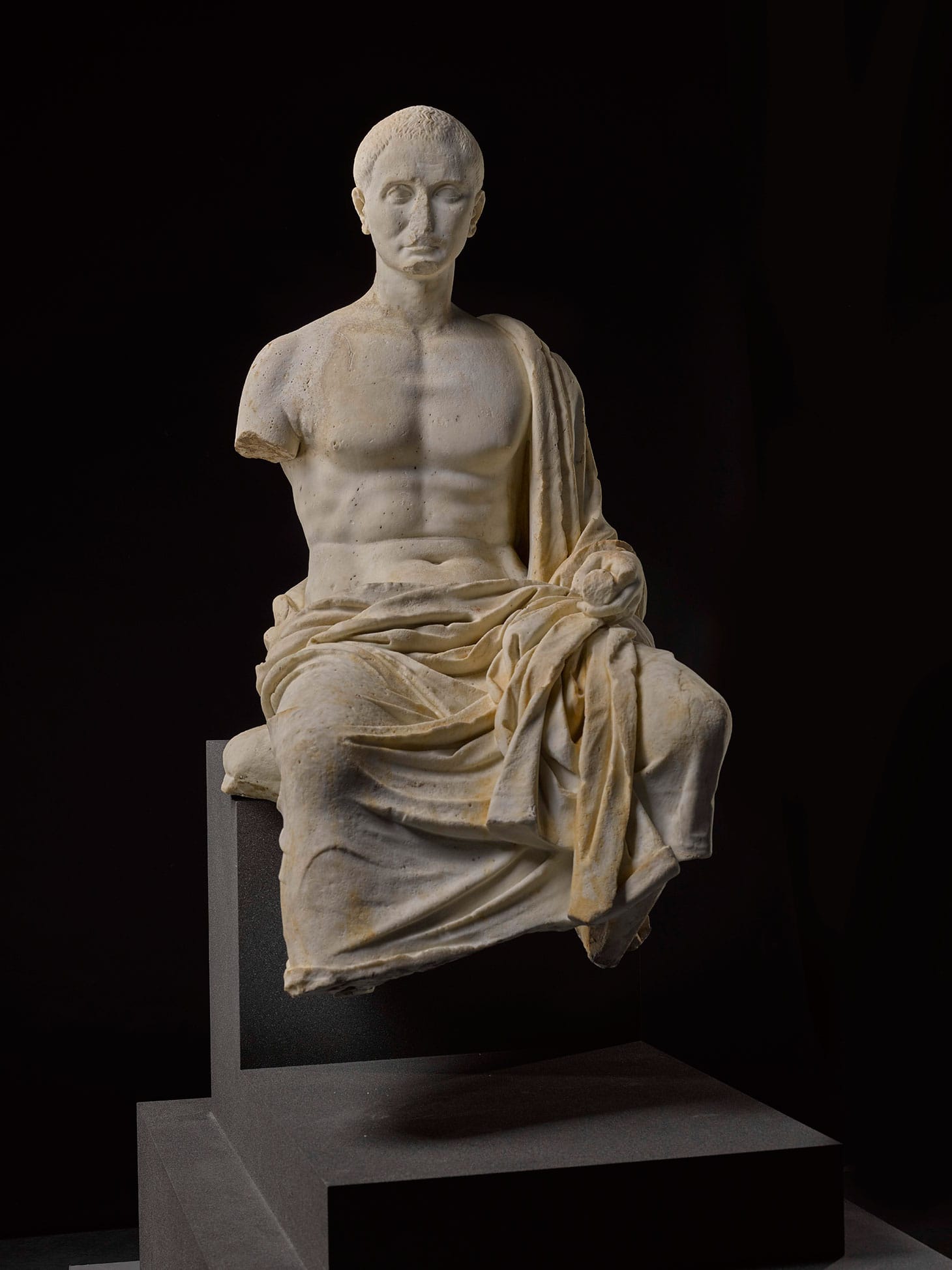 A marble funerary portrait statue of a Roman poet, late Republican/Augustan, 2nd half of the 1st Century BCE, composed of two parts joined at the hips and hollowed out, seated on a cushion in a contemplative attitude and holding a scroll in his left hand, a signet ring on his left hand, his himation draped over the lower part of his body, left shoulder, and left forearm, his head turned slightly to his right, the face with high cheek-bones, fragmentary aquiline nose, deep-set eyes, and furrowed brow, his short cropped hair radiating from the crown, his right foot formerly dowelled on, right shoulder restored, height 115 cm., height of head 25 cm. (image courtesy Sotheby's)