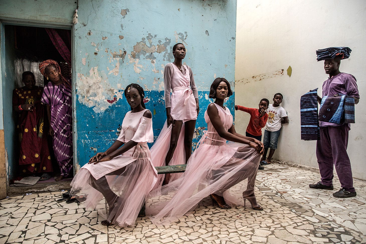 Finbarr O'Reilly, "Dakar Fashion" (2018): Diarra Ndiaye, Ndeye Fatou Mbaye, and Mariza Sakho model outfits by designer Adama Paris, in the Medina neighborhood of the Senegalese capital, Dakar, as curious residents look on (© Finbarr O'Reilly)