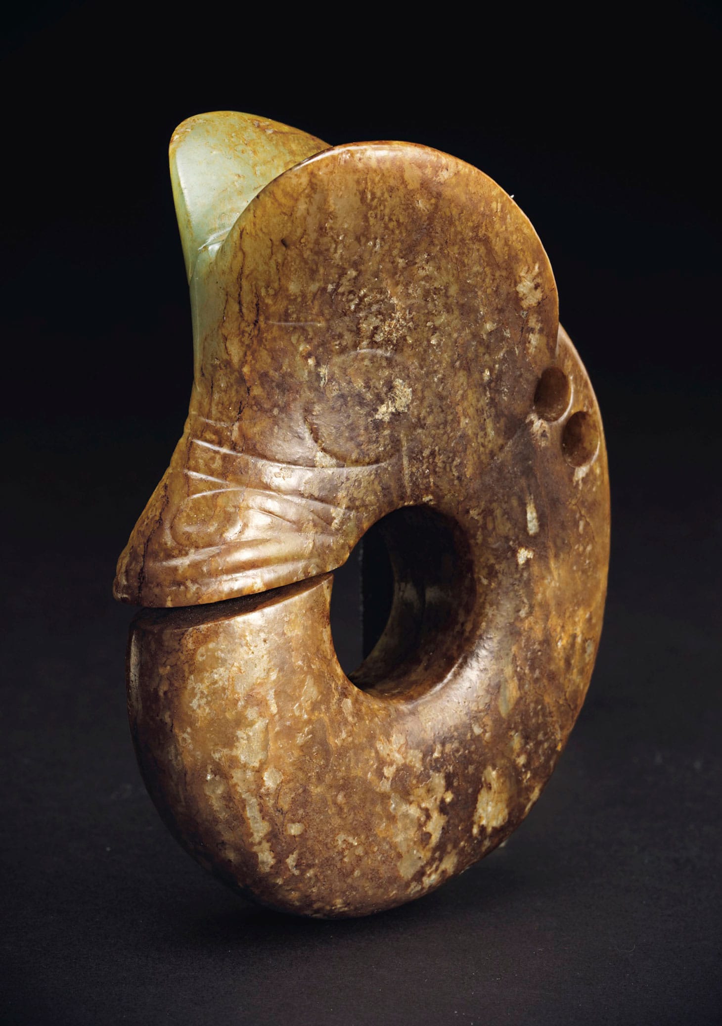 A large archaistic pale green and russet jade carving of a "pig-dragon," China, carved in the Hongshan-style as a coiled stylized mythical animal, pierced with two circular apertures on one side, the stone of a pale yellowish green and russet tone 5 1/8 inches high (image courtesy Christie's)