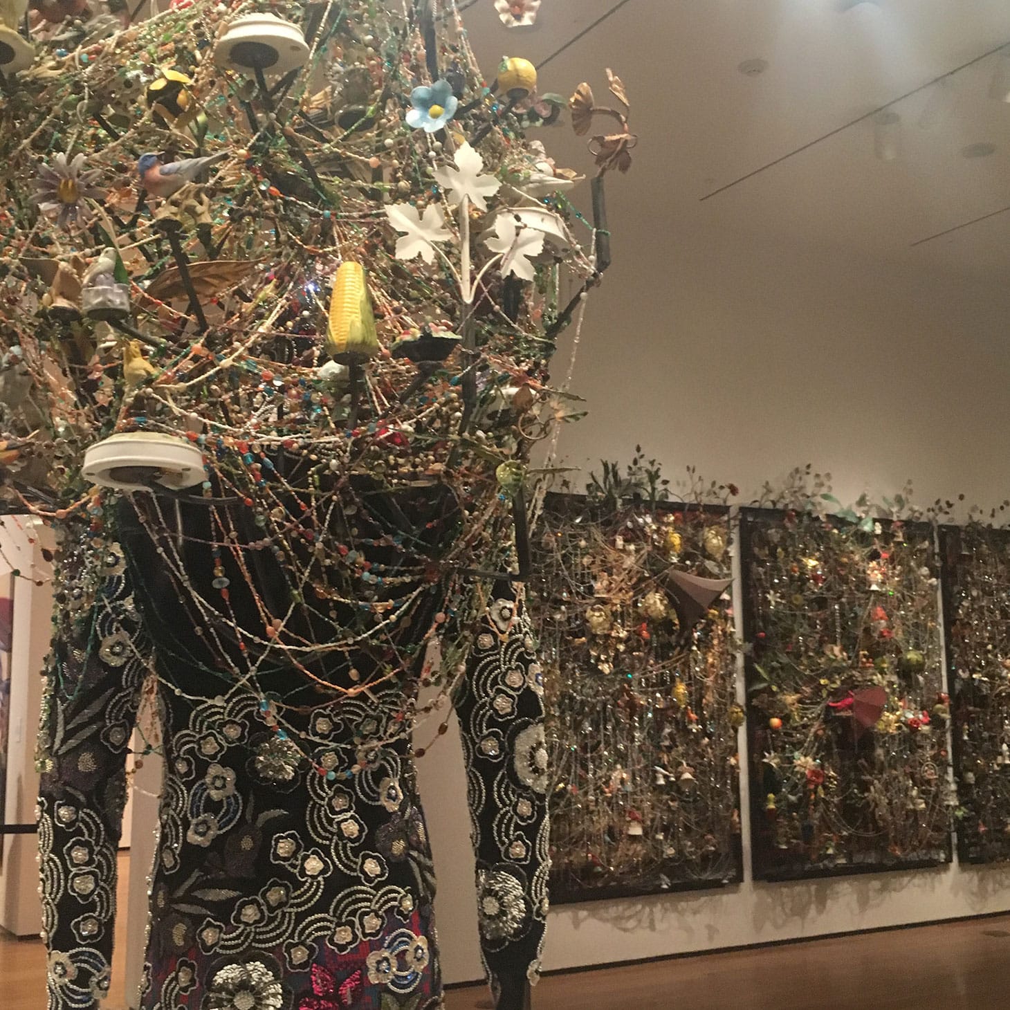 Nick Cave, detail of “Soundsuit” (2013) across from “Wall Relief” (2013), mixed media, including ceramic birds, metal flowers, afghans, strung crystals, and gramophone