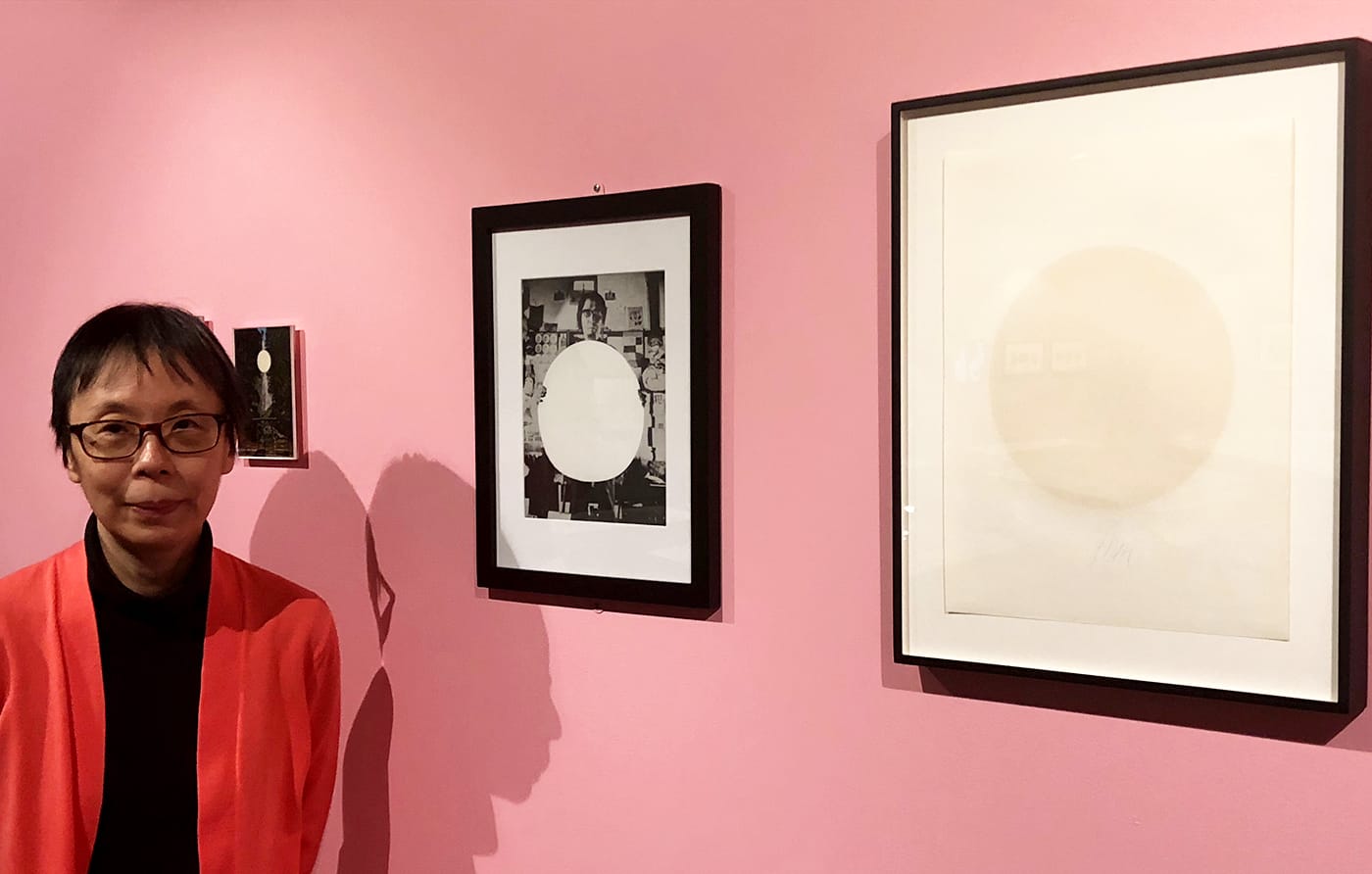 Curator Reiko Tomii with works by Yutaka Matsuzawa featuring the white circles the artist regarded as visual aids for meditation; he intentionally displayed the white-ink-on-paper silkscreen on the right with its back side facing out (photo by the author for Hyperallergic)