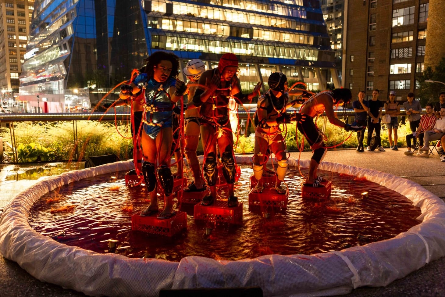 5 performers stand in various postures inside a small pool of water on the high line plinth