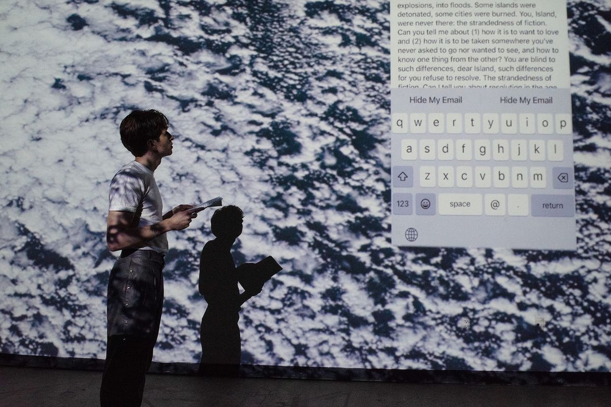 Drew Zeiba Bard MFA Writing class of 2024 performing their work “The Mirror”. Drew is reading in front of a black-and-white p