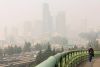 A woman walks across the Jose Rizal Bridge as a blanket of wildfire smoke obscures the view of the Seattle skyline, Friday,