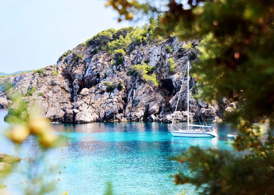Sailing boat on the water with rocky landscape and deep blue water - best beaches in Spain