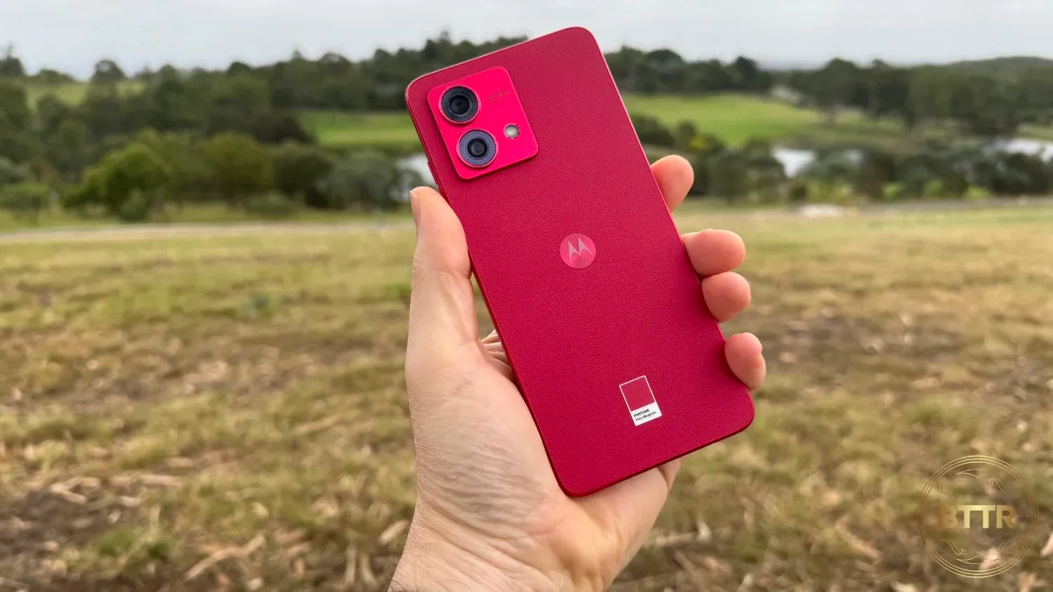 The Motorola G84 being held with rolling hills in the background