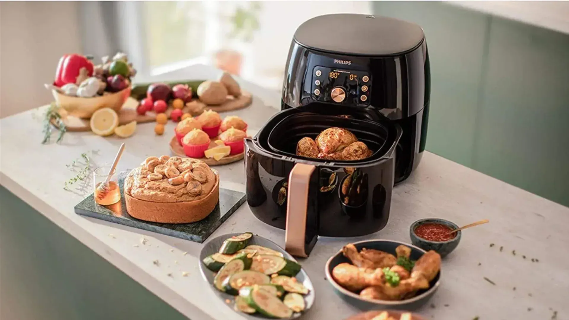 A Philips air fryer on a kitchen bench surrounded by plates of food