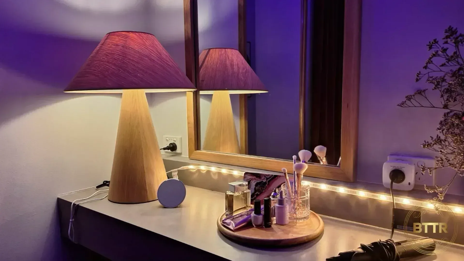 The Amazon Echo Dot on a bench in front of a mirror, next to a lamp.