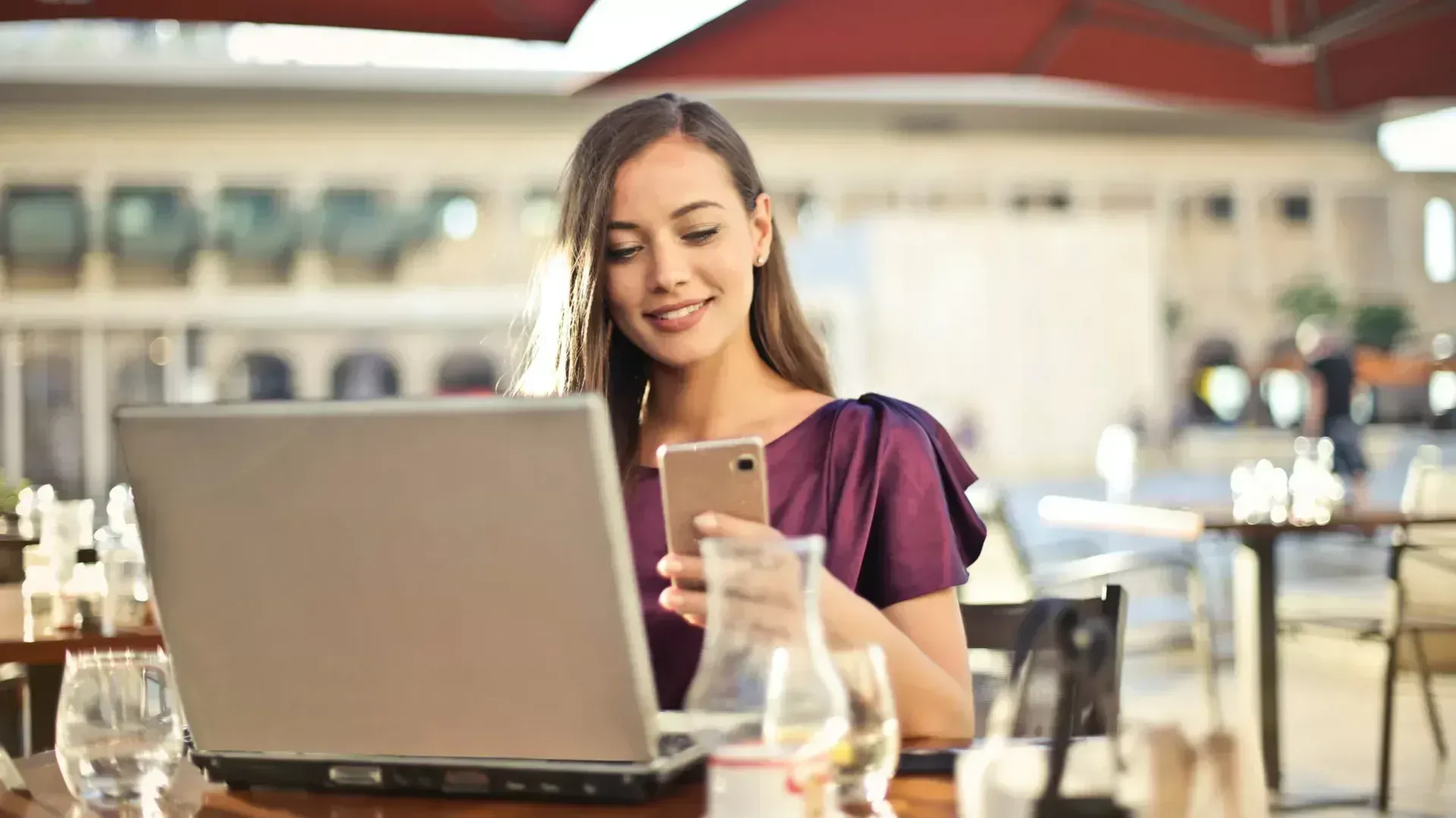 A woman in a restaurant looking at her phone while she works on one of the best laptops.