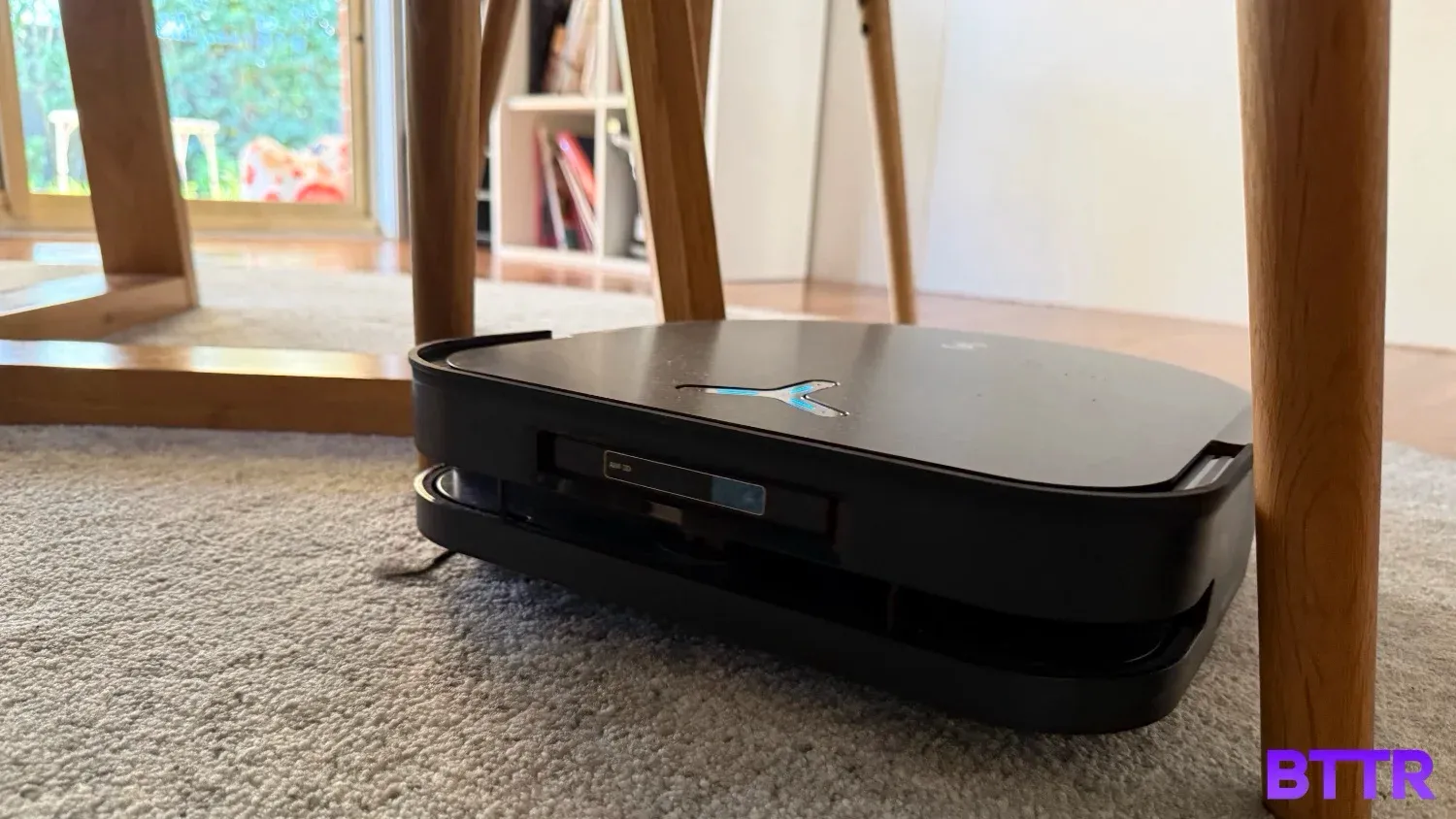 The Deebot X5 Pro Omni vacuuming carpet under a chair