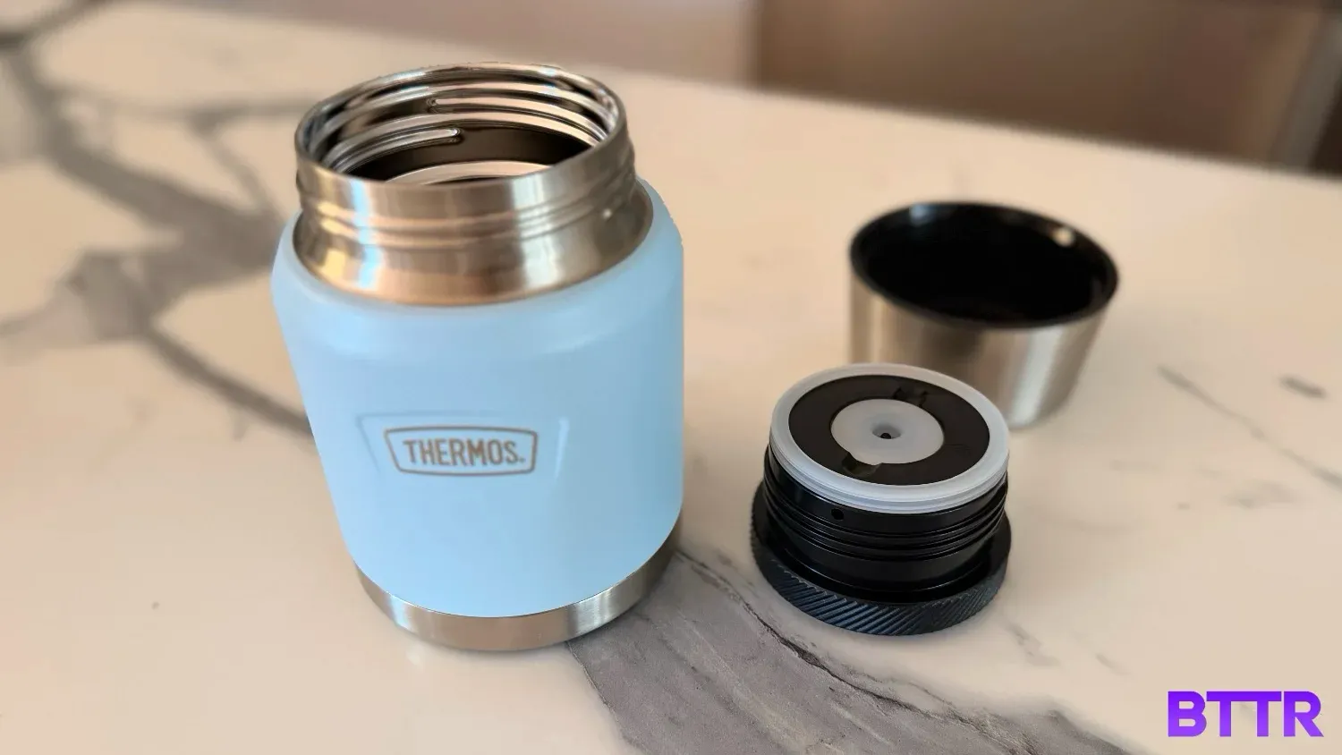 The thermos icon series food jar opened with the lid upside down on a counter next to the jar