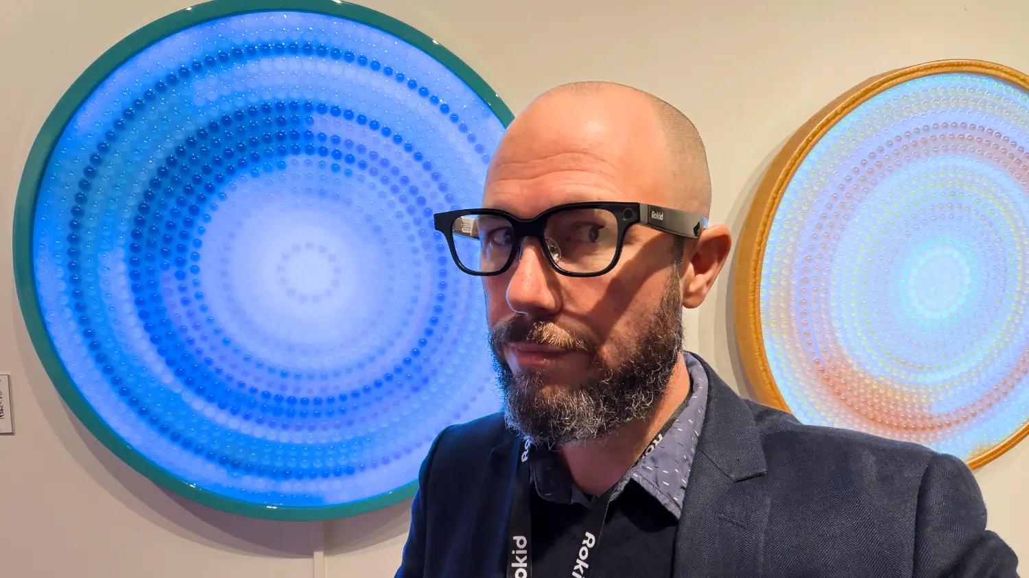 BTTR founder Nick Broughall wearing the Rokid AI glasses in front of some artwork.