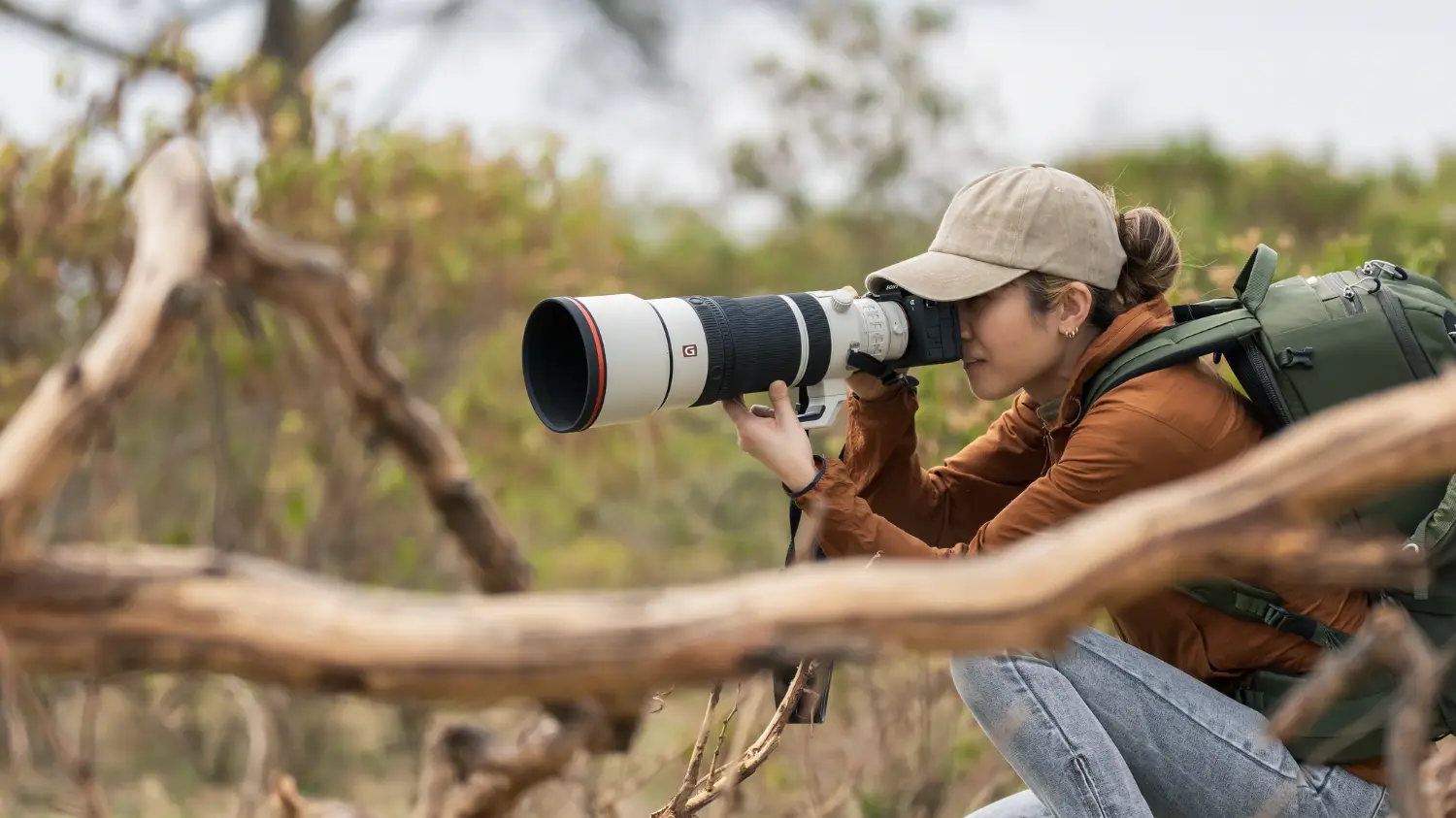 a woman in scrubland taking a photo using the FE 100-400mm F4.5 GM OSS lens