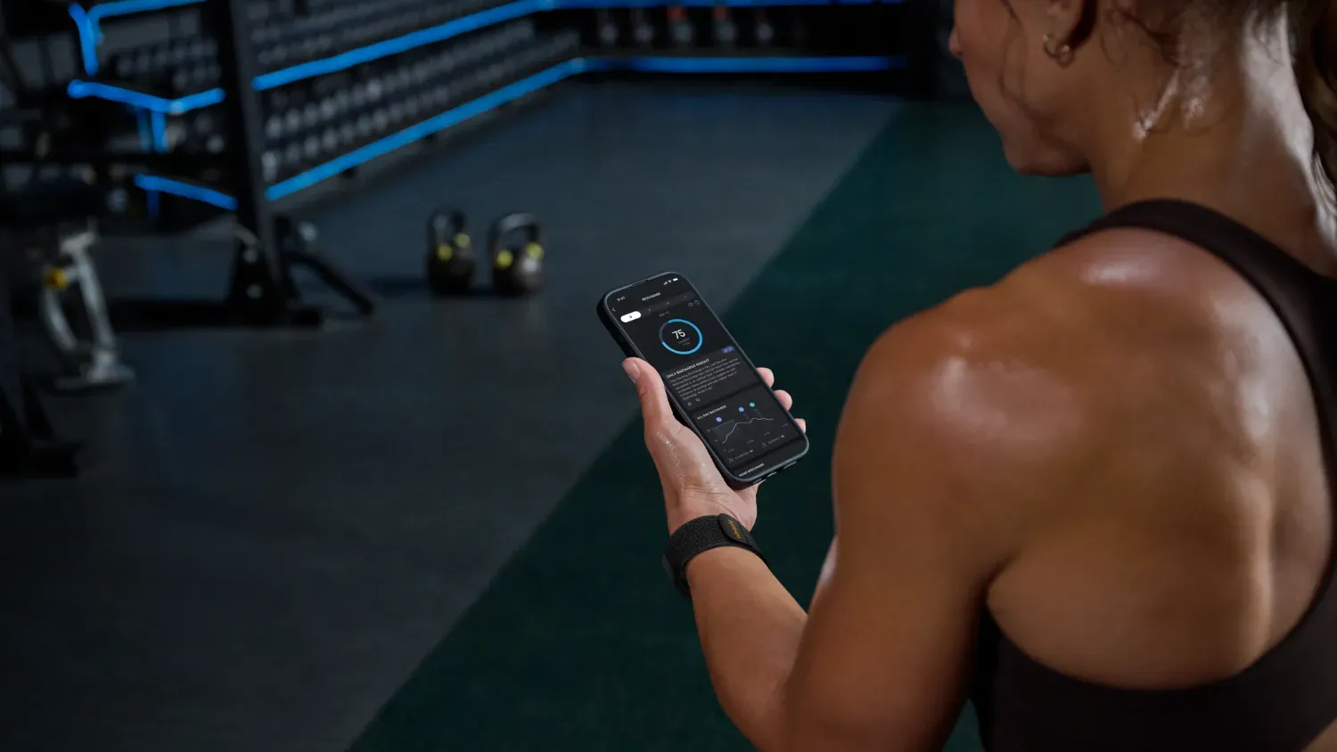 a woman in the gym wearing the Helio Strap and checking her phone