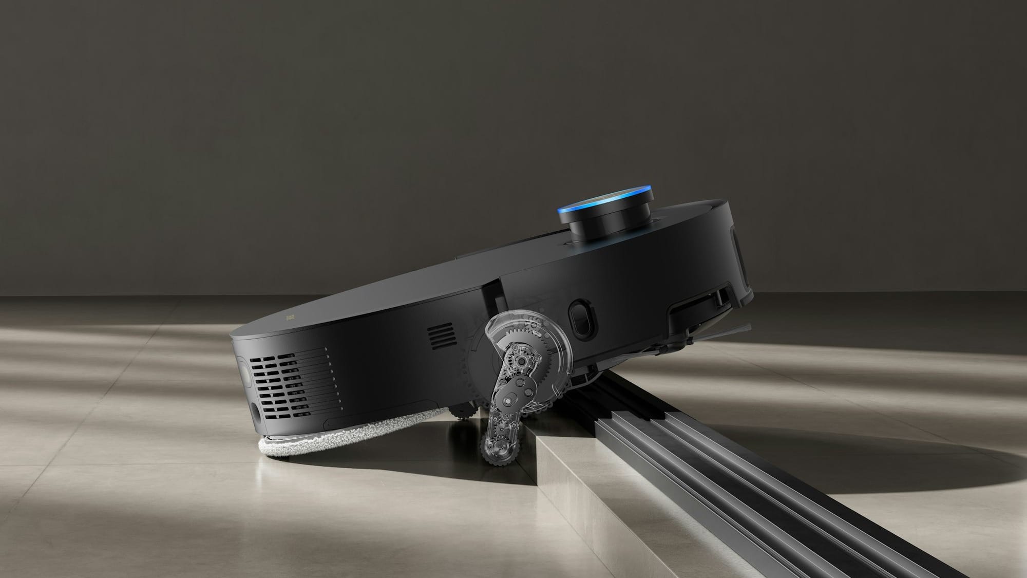 A black robot vacuum cleaner on a light gray floor stepping over a ledge