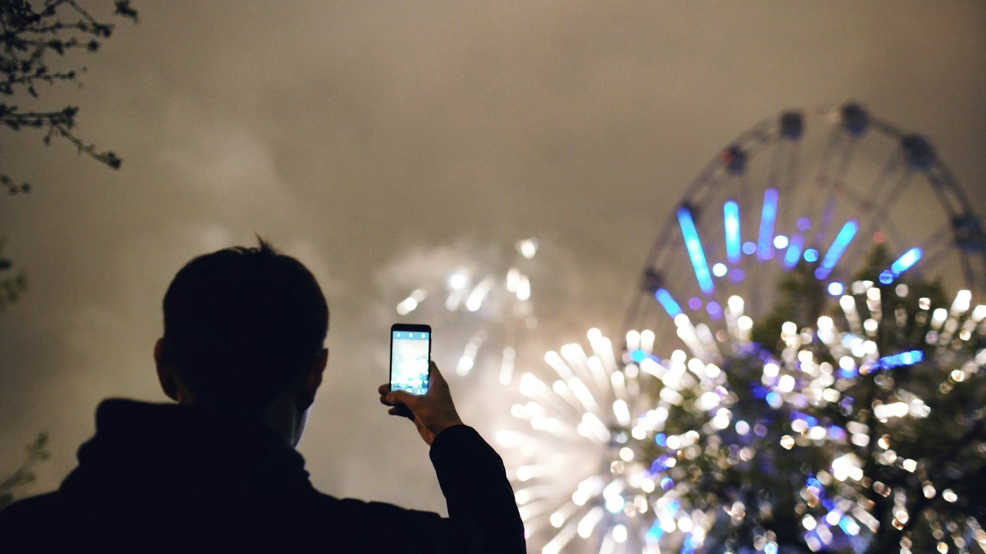 Person records fireworks with a smartphone at night.