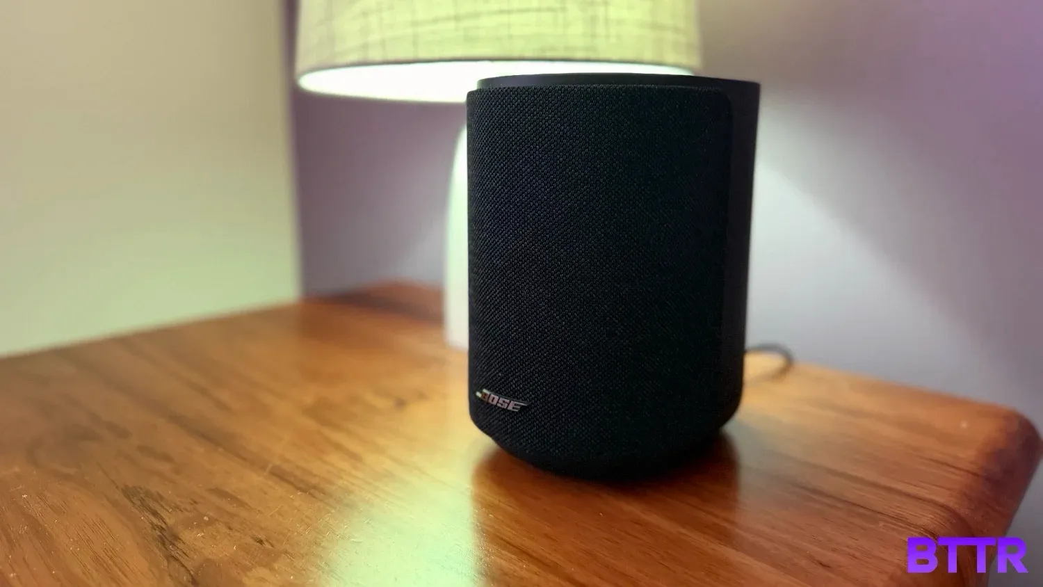 The Black Bose Lifestyle Ultra speaker on a bedside table with a lamp
