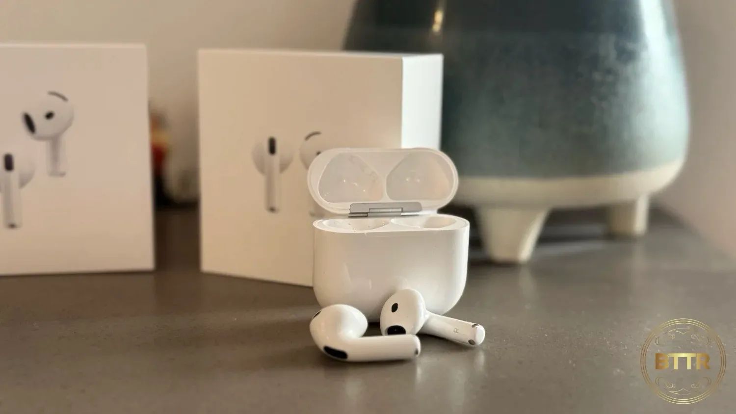 The Airpods 4 on a bench infront of the box and a pot plant