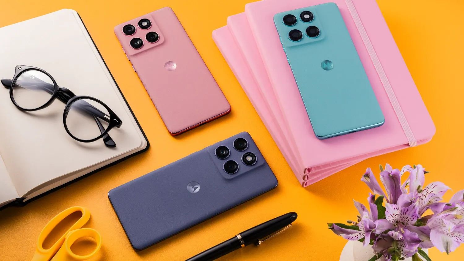 Moto edge 60 fusion models on an orange background with a notebook and pen and scissors and flowers