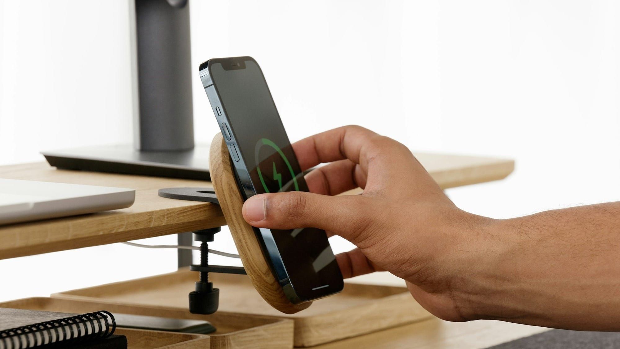 A hand putting an iPhone on a wireless charger at a desk