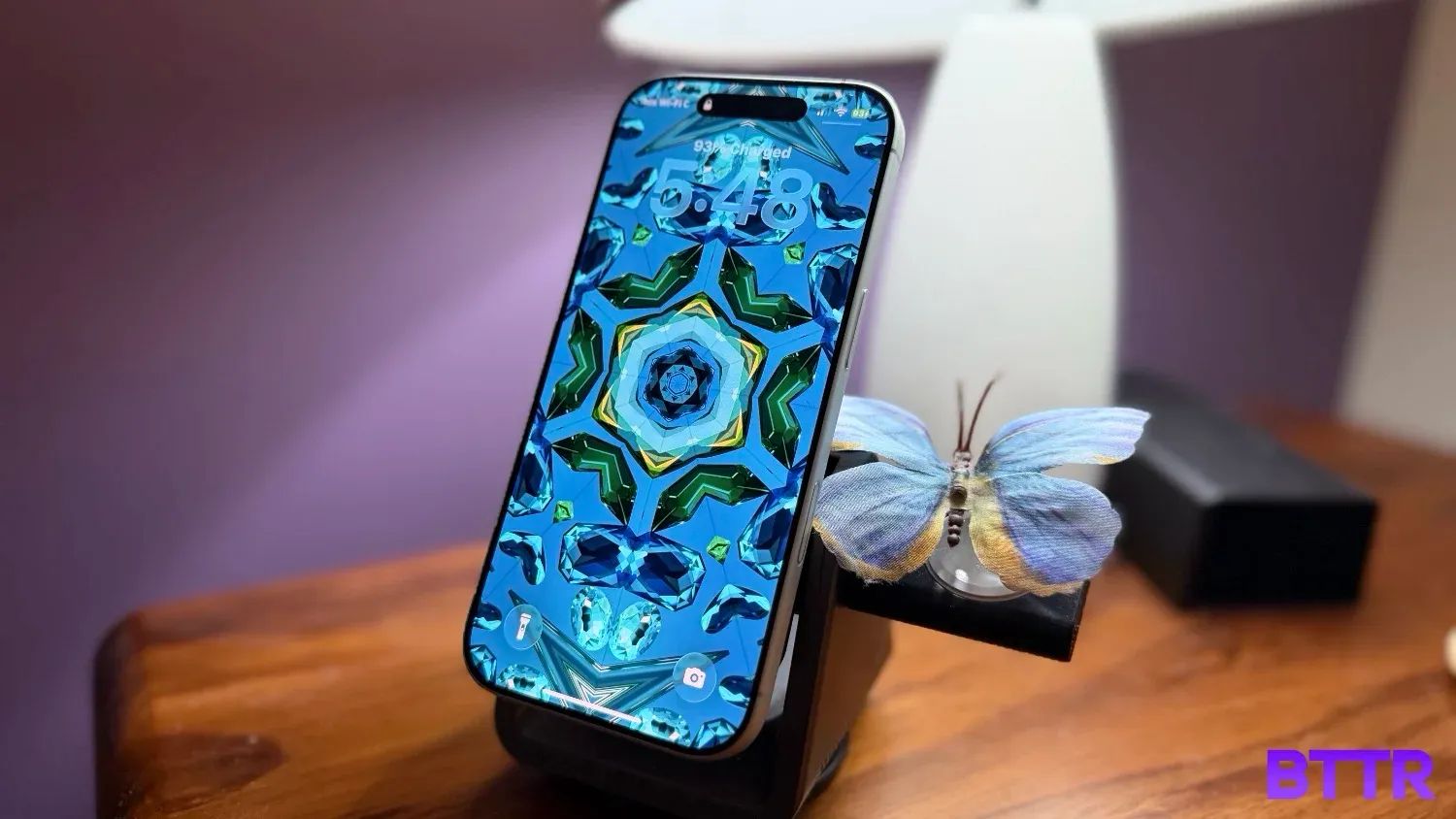The iPhone 17 on a charger with a butterfly and a lamp in the background