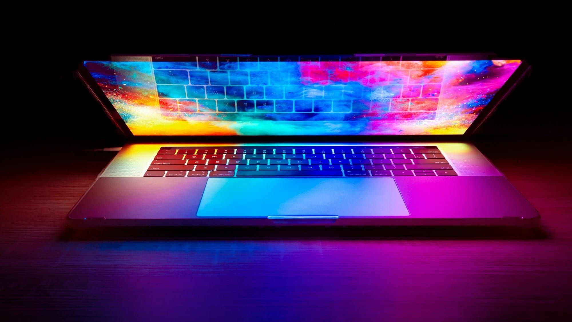 A laptop with a colourful screen in a darkened room