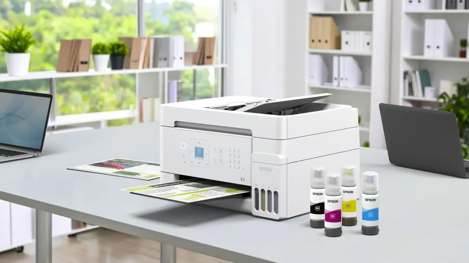 The Epson ET-4900 on a desk with ink and several laptops on the same desk.