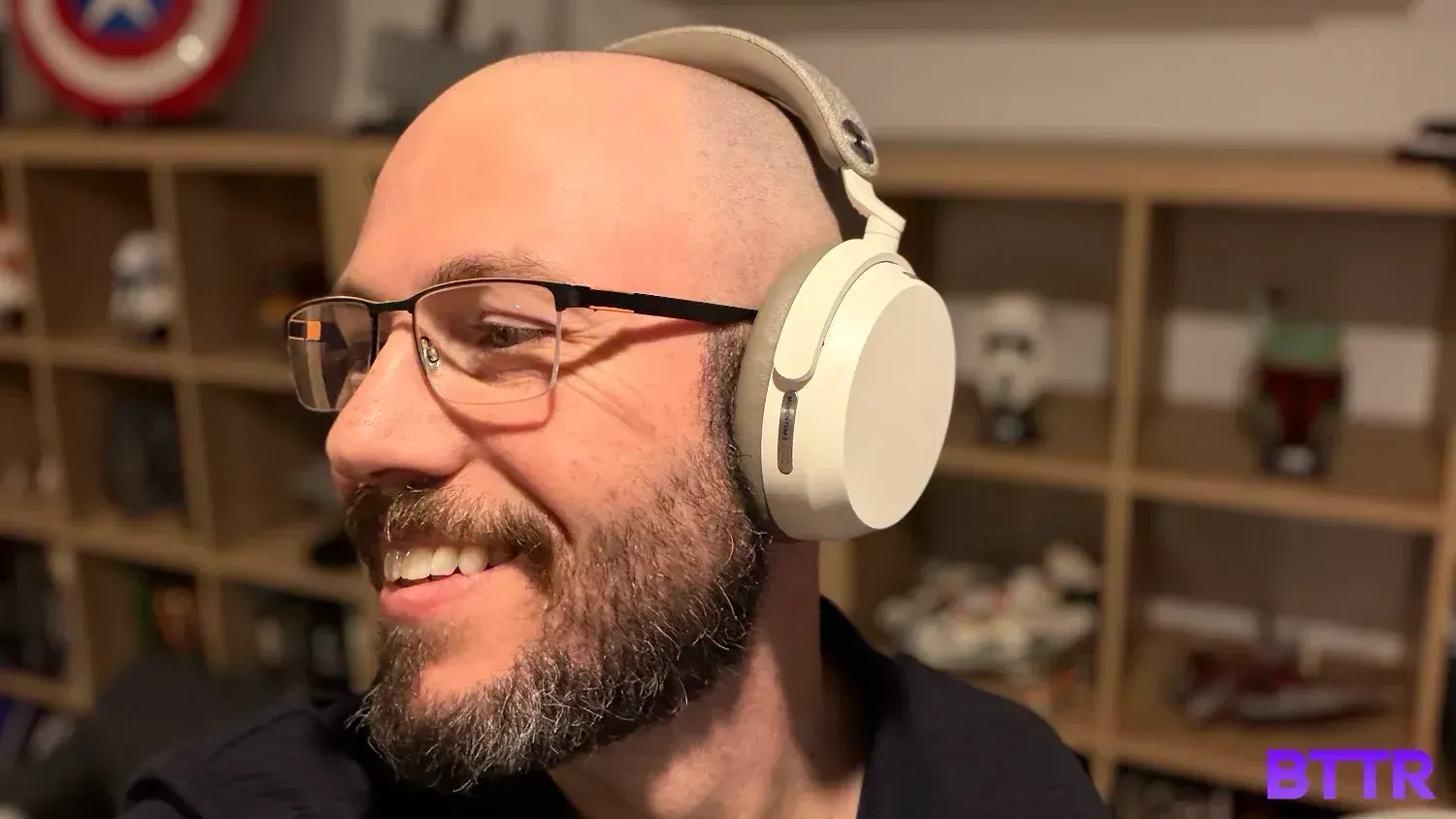 A bearded man smiling while wearing the Sennheiser Momentum 5 in front of some Lego-filled shelves