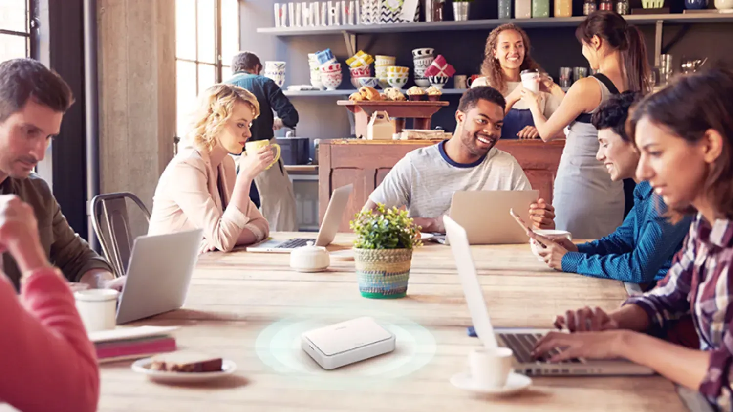 The DBR-330-G 5G AX3000 Wi‑Fi 6 Mobile Hotspot on a table in a cafe surrounded by people on laptops