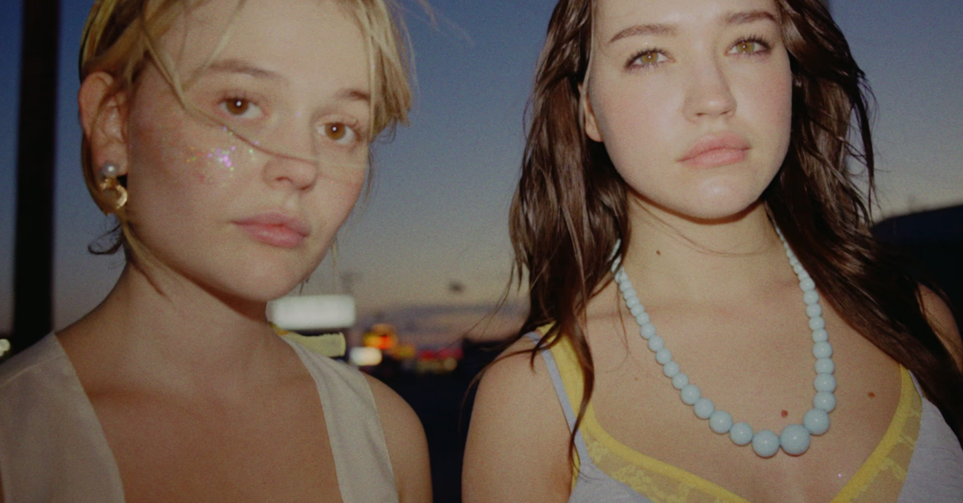 Marie, wide-eyed with glitter on her cheeks and Luna with lacey top and blue bubble pearl necklace stand in the dying light of a highway truck stop.