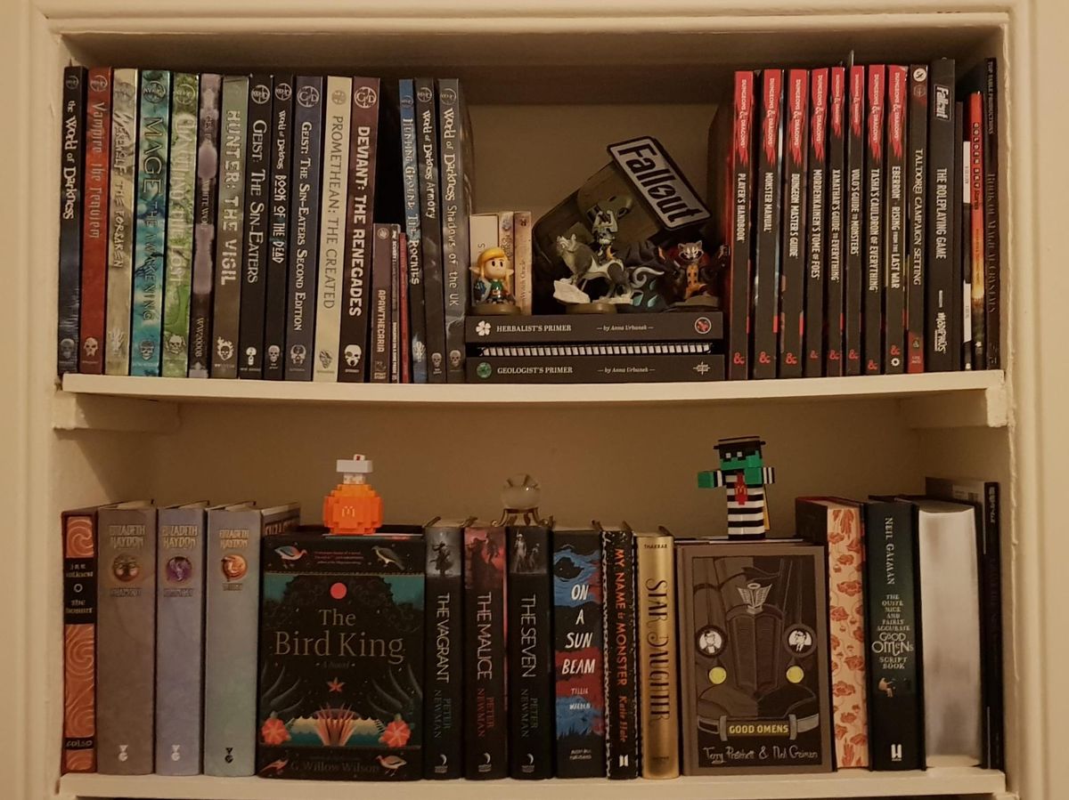 A very neat shelf with fiction hardbacks on the lower shelf and RPG rulebooks on the top. The RPG guides are mostly for Chronicles of Darkness and D&D. Piles of custom dice sit in the centre.
